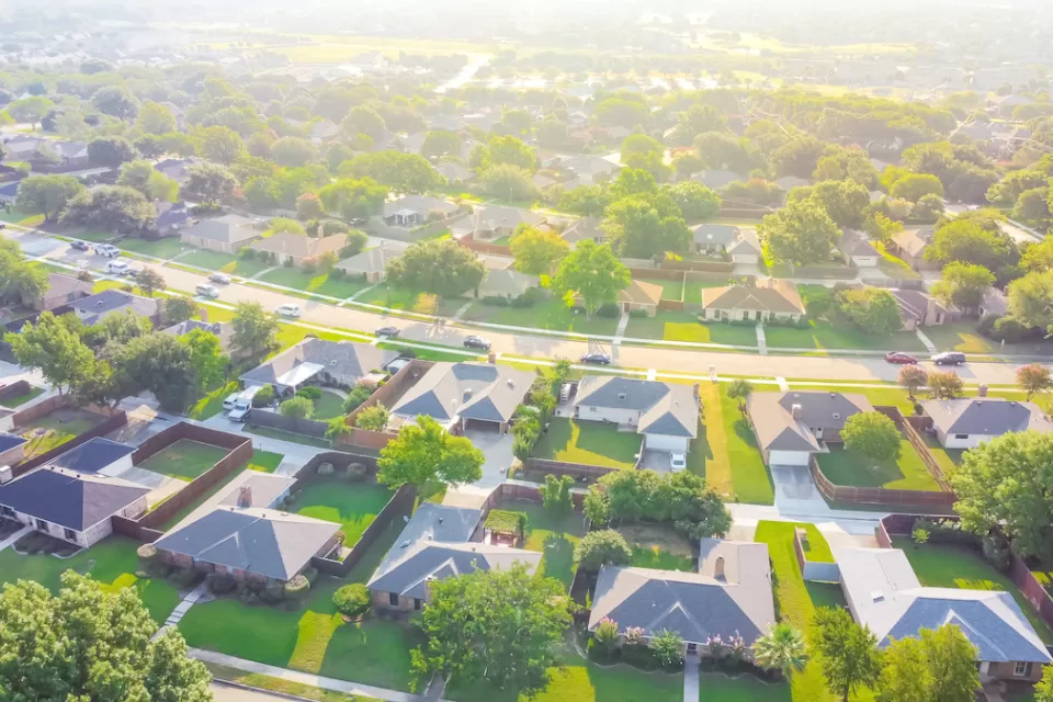 Aerial view of suburb outside Dallas, Texas with large single-family houses with enclosed backyards and green lawns.